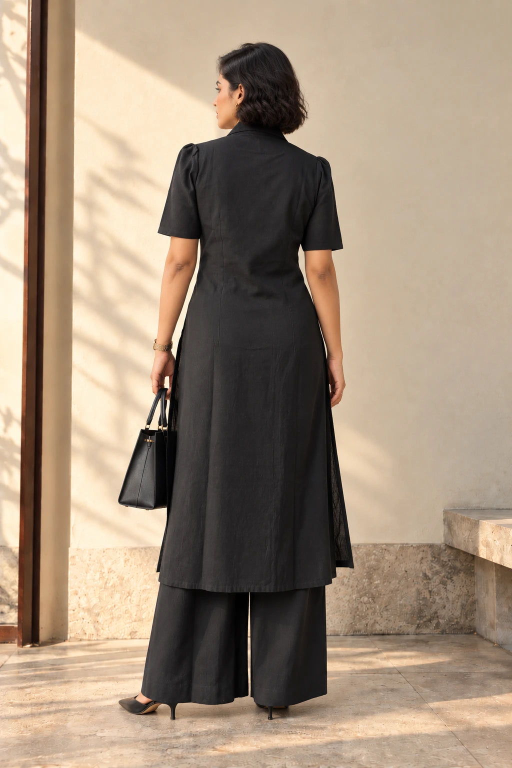 Back view of black coat-style kurta set showing puff sleeves, shaped seams, side slits and full-length palazzos