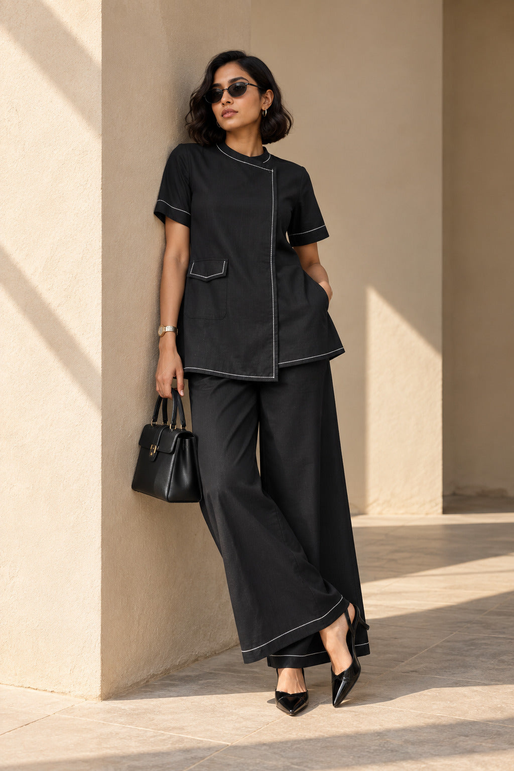 Close-up of black cotton kurta showing band collar, asymmetric overlap front, flap patch pocket and white contrast stitching